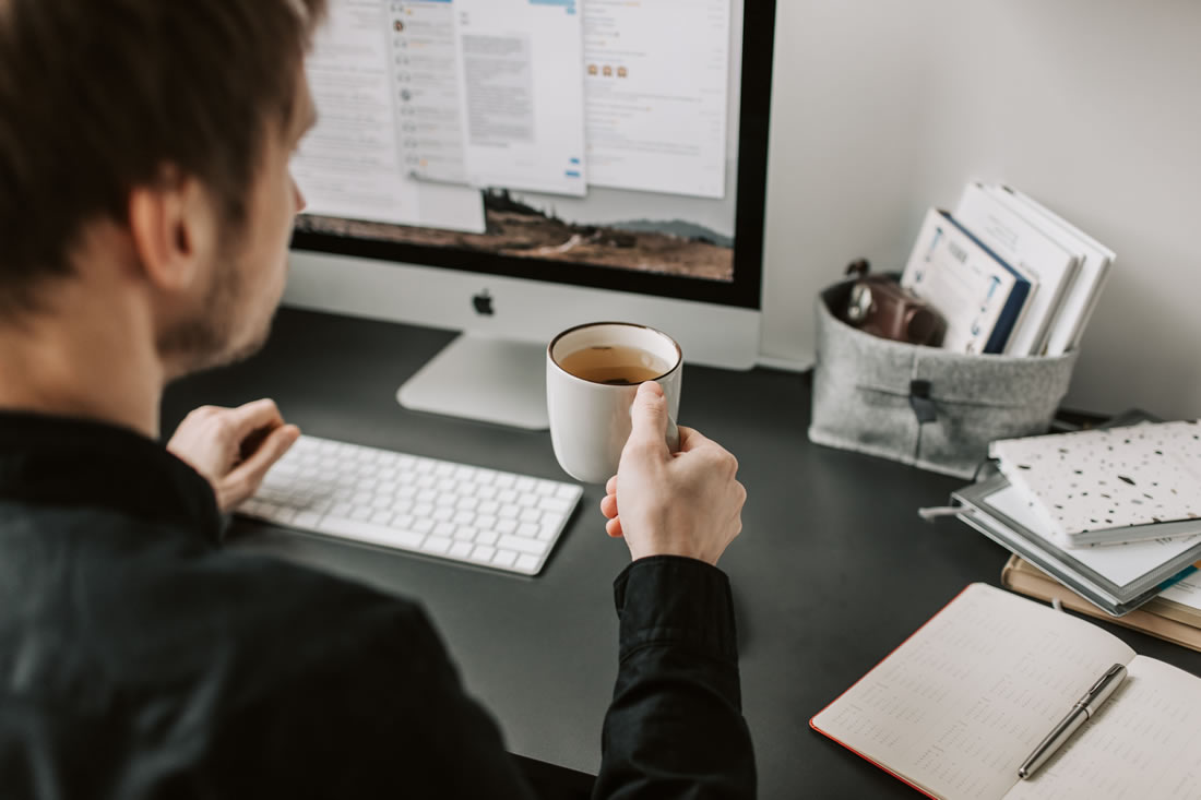 A man working on a laptop with coffee indoors, illustrating hybrid work and the need for UltraSoftBIS Cloud to support flexible workspace operations